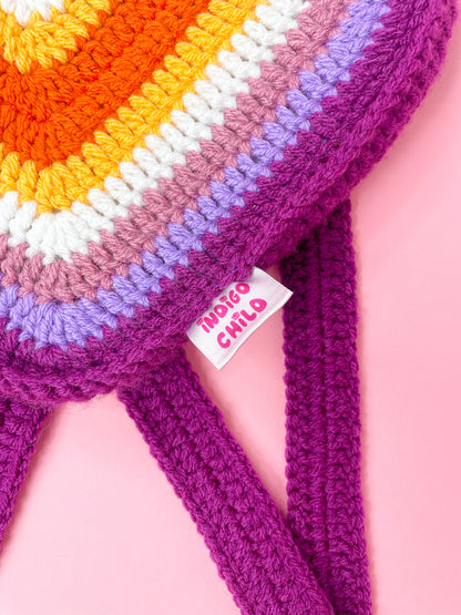 close view of a crochet bag shaped like a heart in lesbian flag colours with an Indigo Child tag attached to the side.