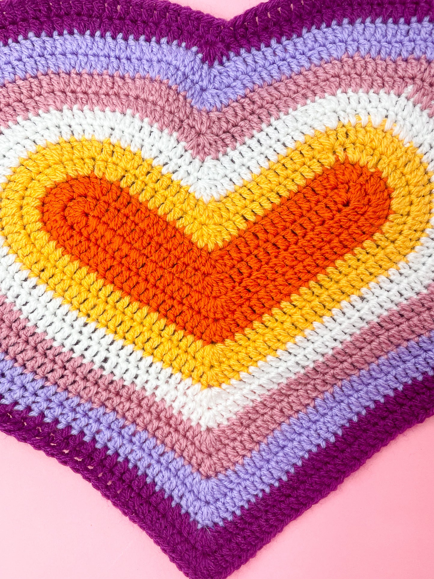 Close view of a crochet heart top in lesbian flag colours showing the crochet stitches and details.