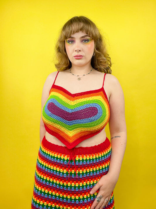 A woman wearing a vibrant rainbow heart shaped top with a matching skirt and makeup.