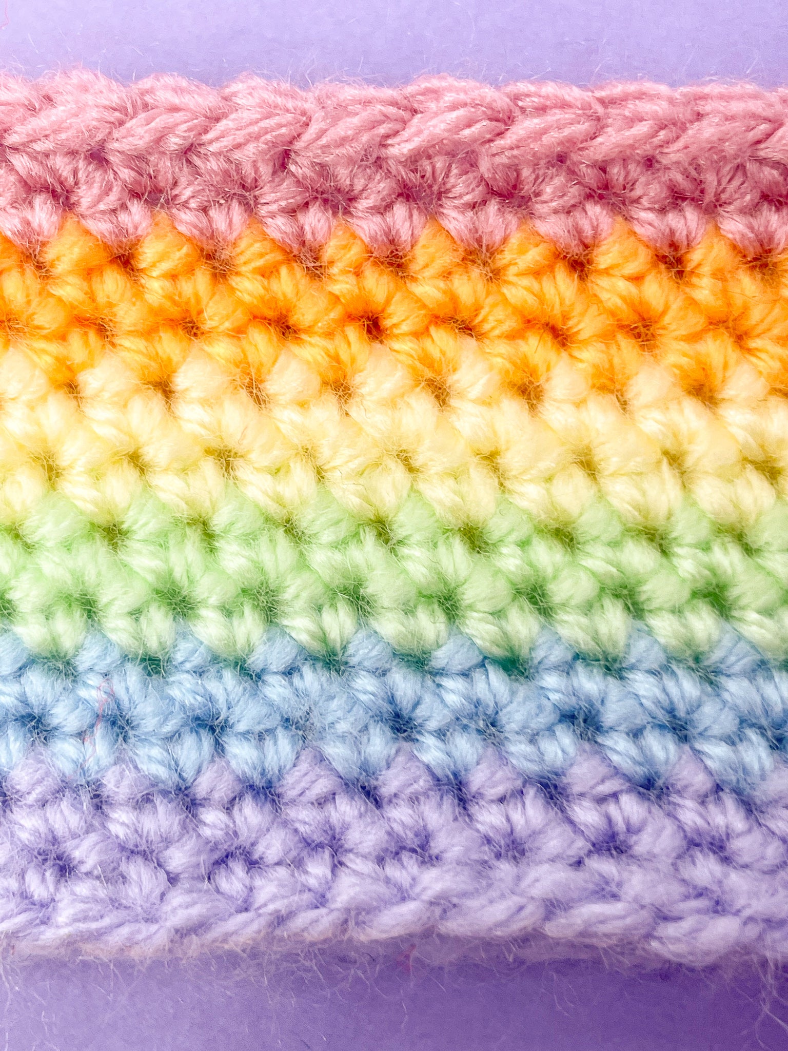 Close up of a crochet headband in pastel rainbow colours with the stitch details.