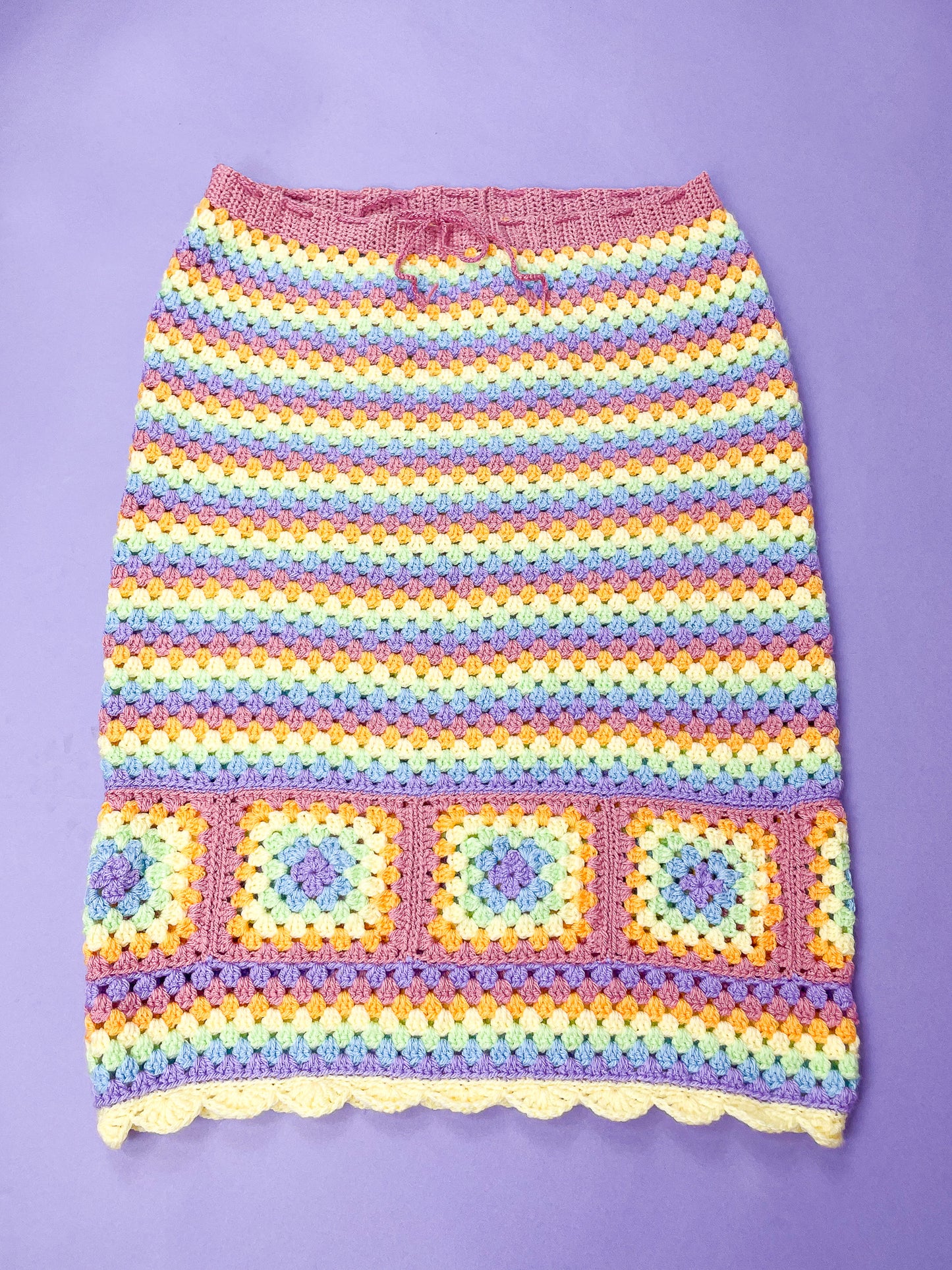 Flat lay of a pastel rainbow skirt with crochet granny squares lying flat on a purple background.