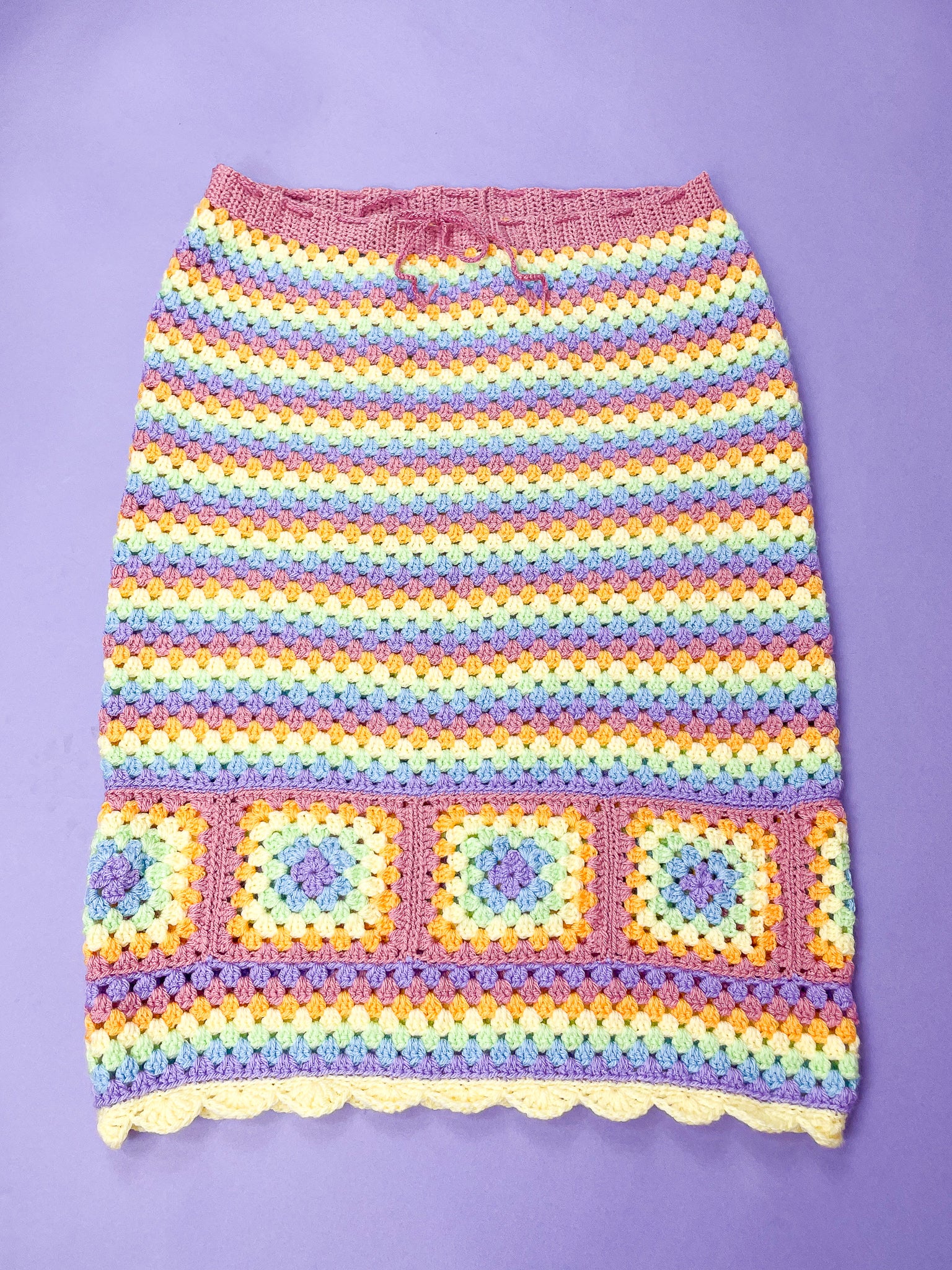 Flat lay of a pastel rainbow skirt with crochet granny squares lying flat on a purple background.