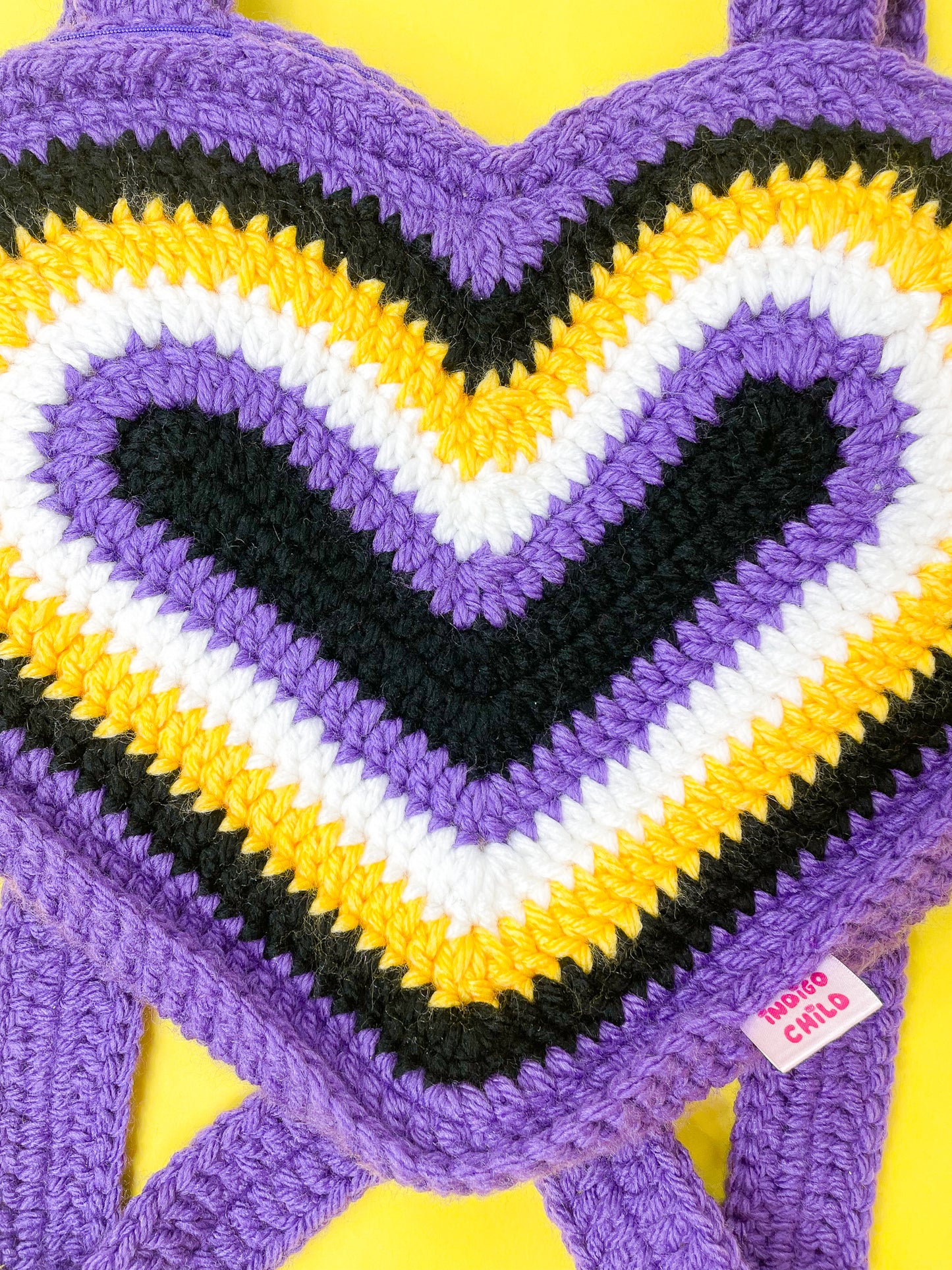 Close view of a heart shaped bag in non-binary flag colours showing the crochet stitches.