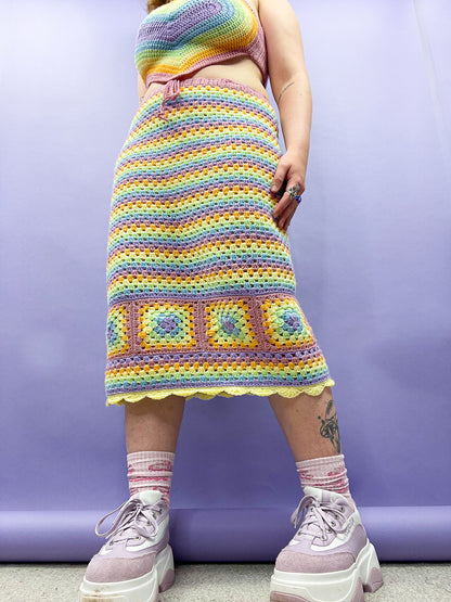 Below view of a woman wearing a crochet midi skirt in pastel rainbow colours with a matching top and lilac platform trainers.