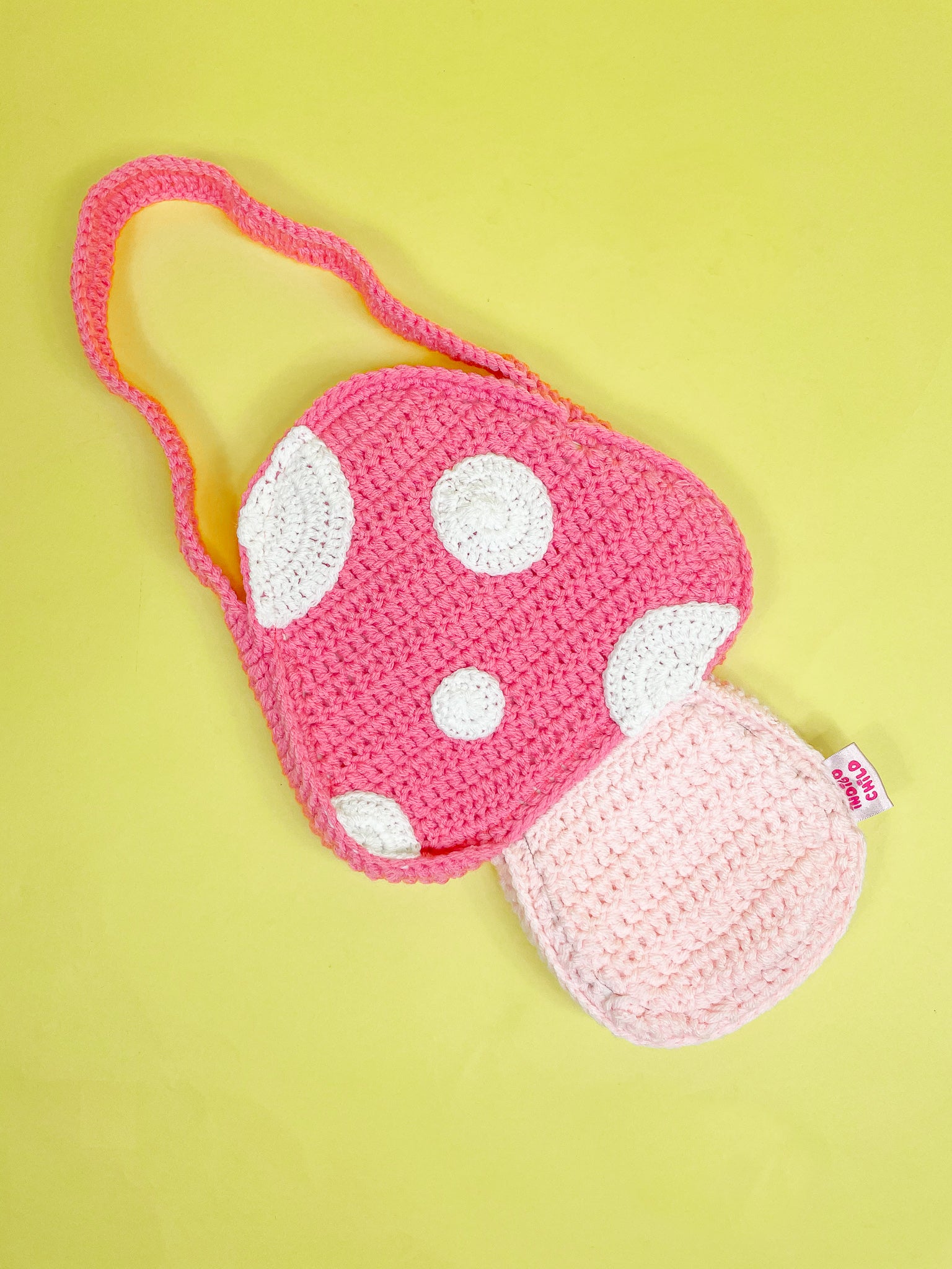 A mushroom shaped bag in pink lying sideways on a yellow background.