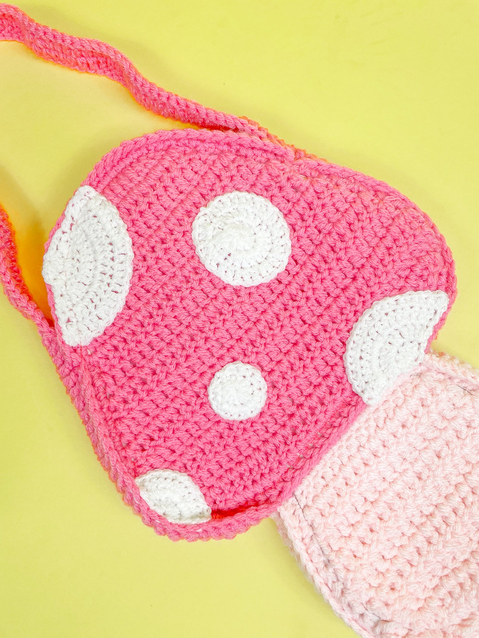 Close view of a toadstool mushroom crochet bag in pink with appliqué dots attached to it showing the crochet stitches.