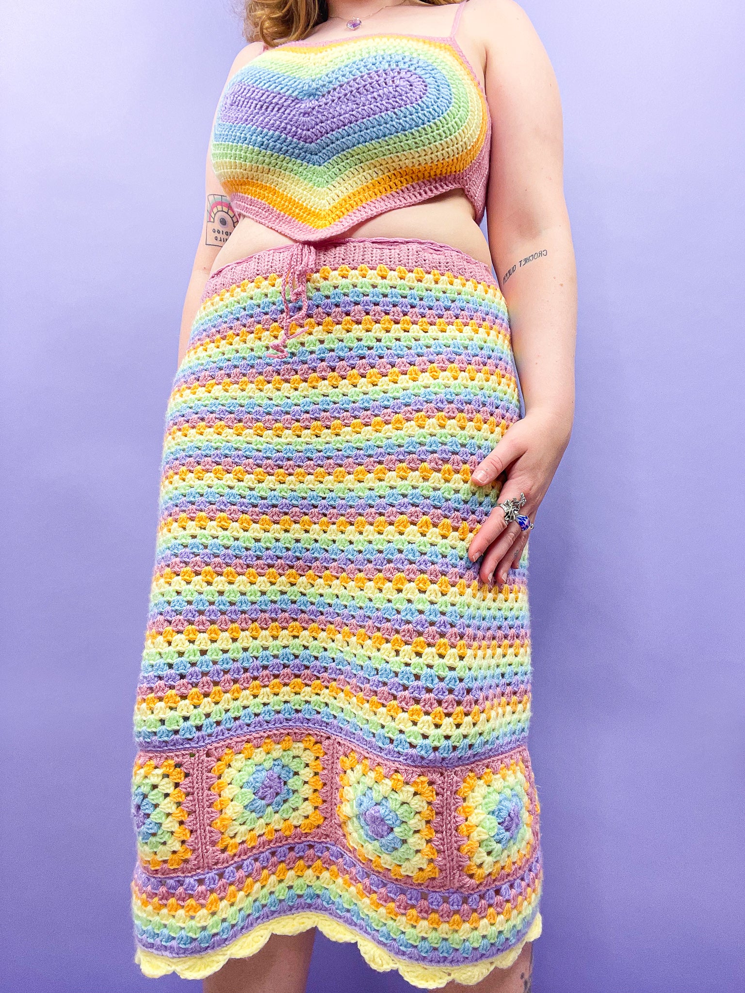 Close below view of woman wearing a pastel rainbow matching top and skirt set in front of a purple background.