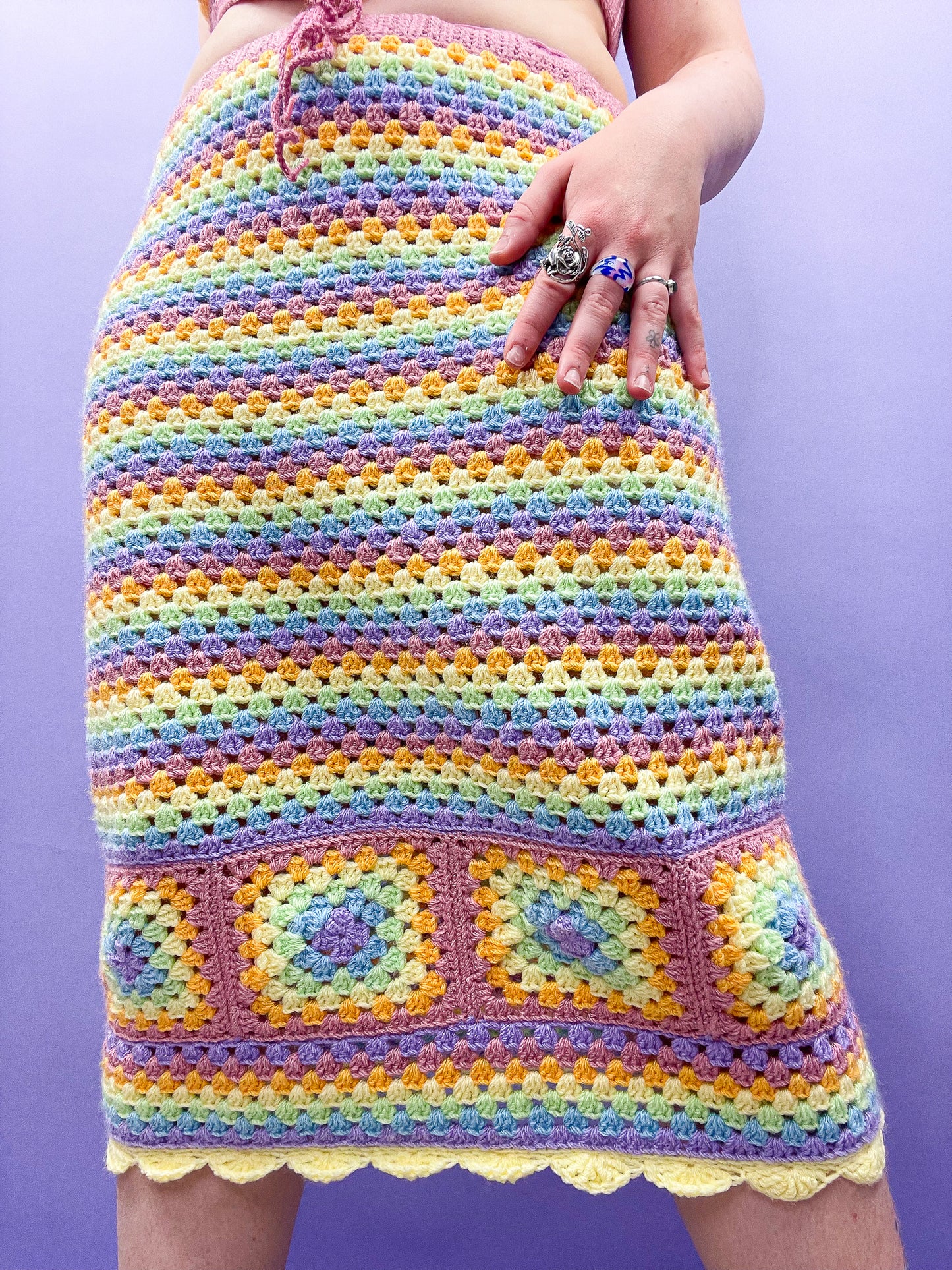 Close up of woman wearing a pastel rainbow midi skirt with a granny square design at the bottom and yellow frilled edges.