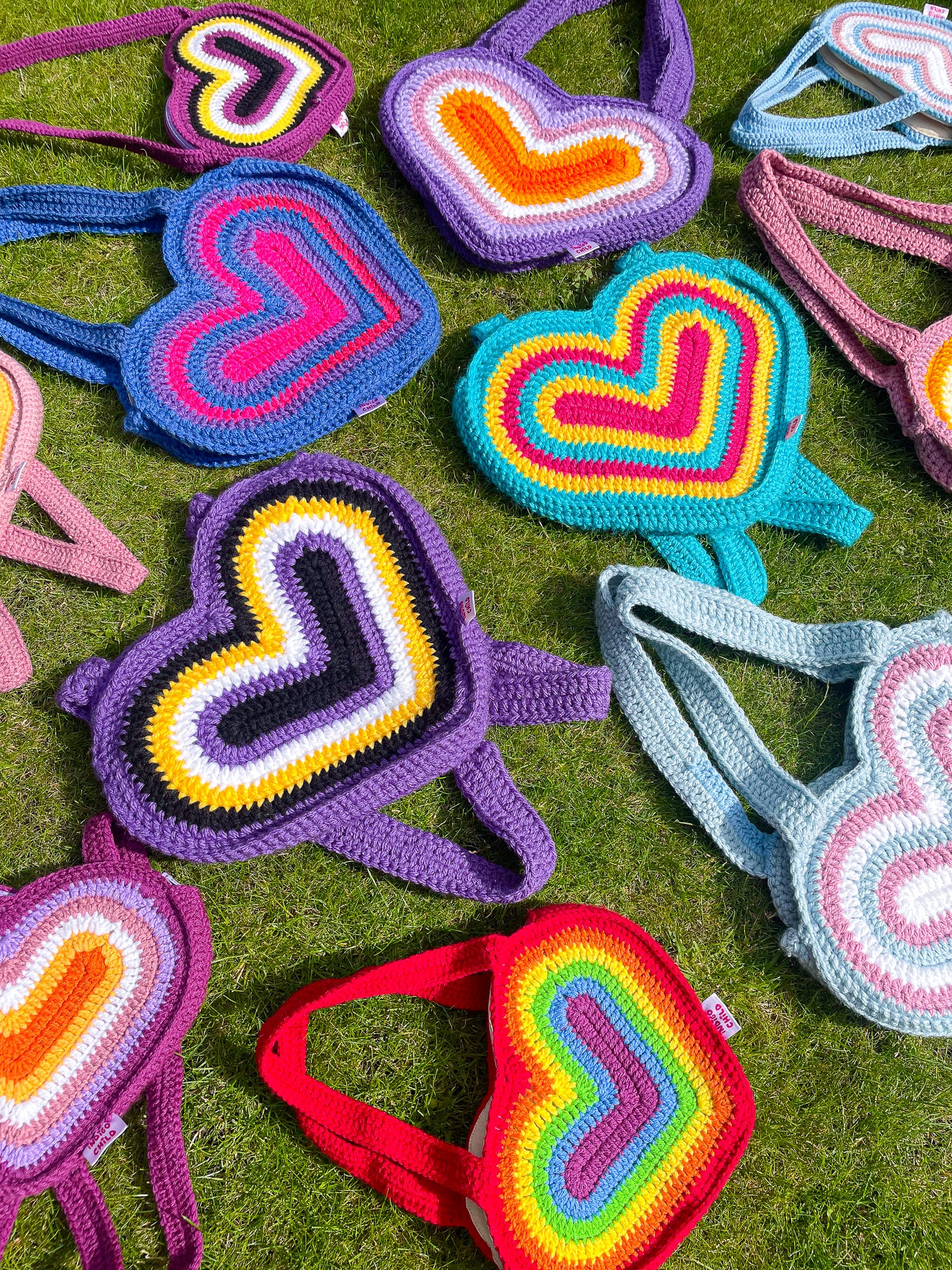 Eleven heart shaped bags in various pride flag rainbow colours, lying together on a patch of grass.