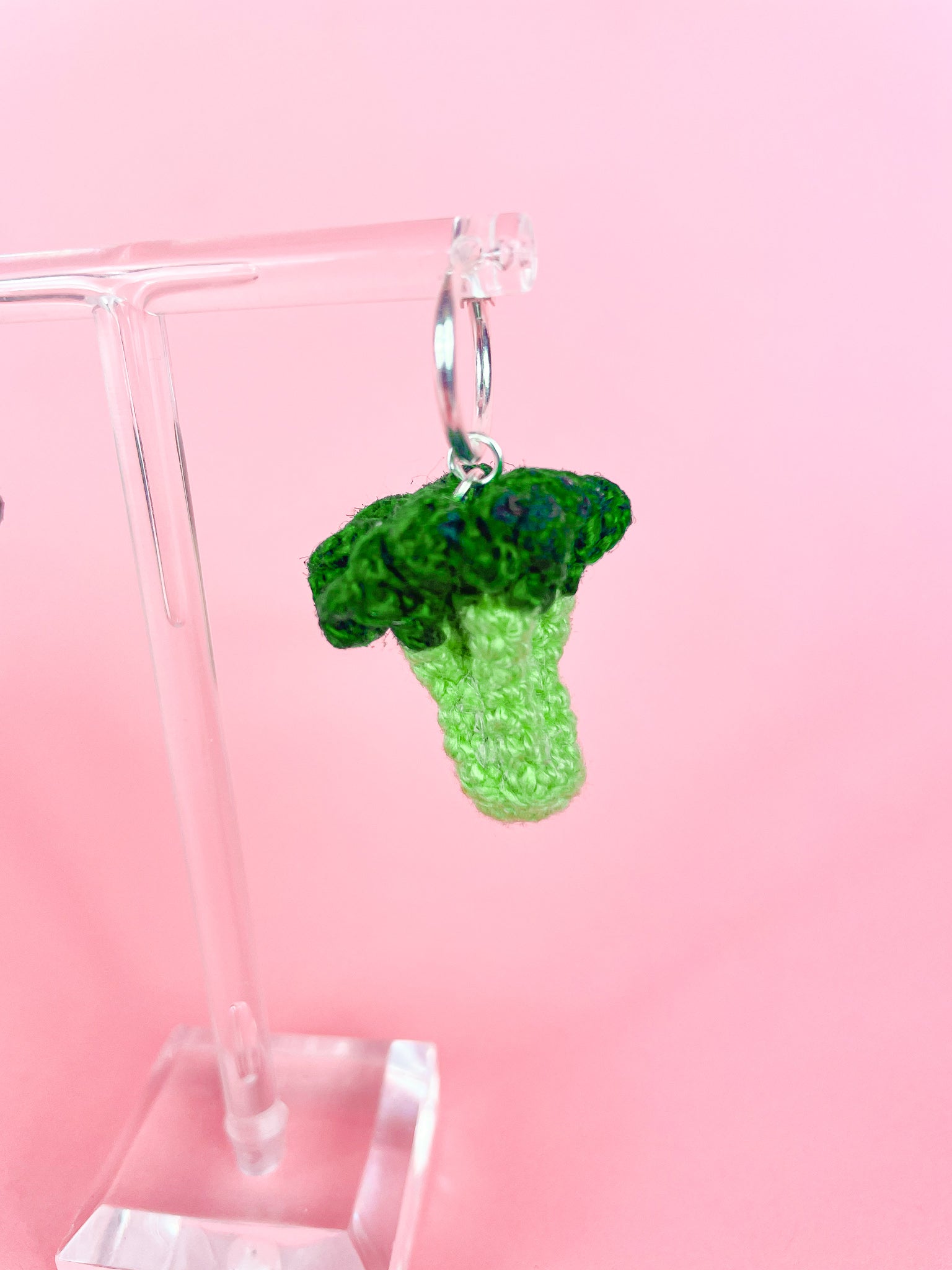 Close view of one hoop earring with a micro crocheted broccoli attached to it hanging on an earring stand.