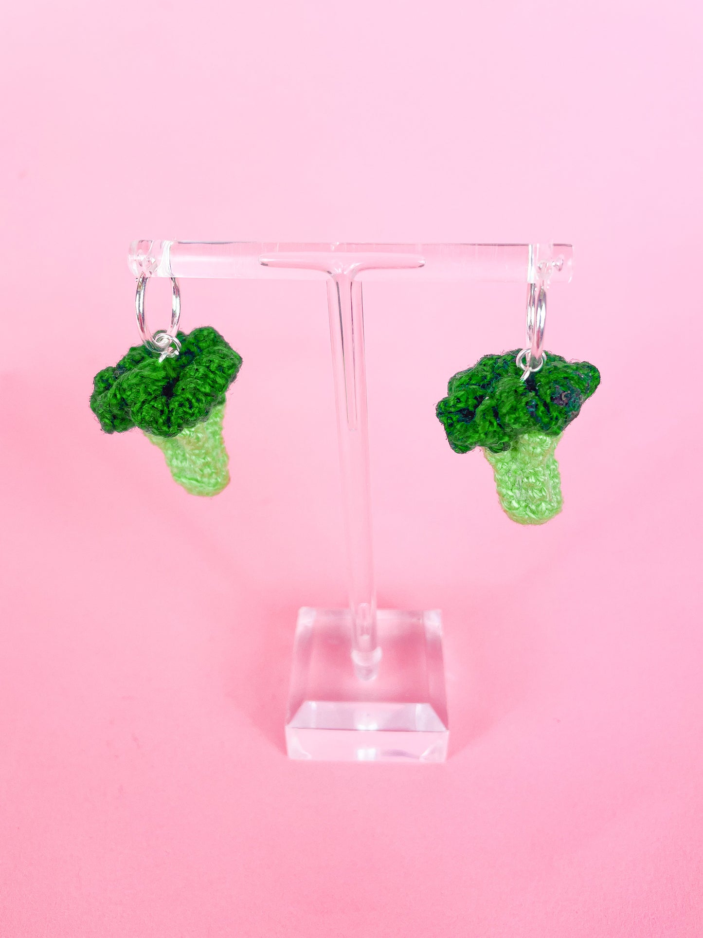 Above view of a pair of crochet broccoli earrings attached to silver hoops hung up on an earring stand.