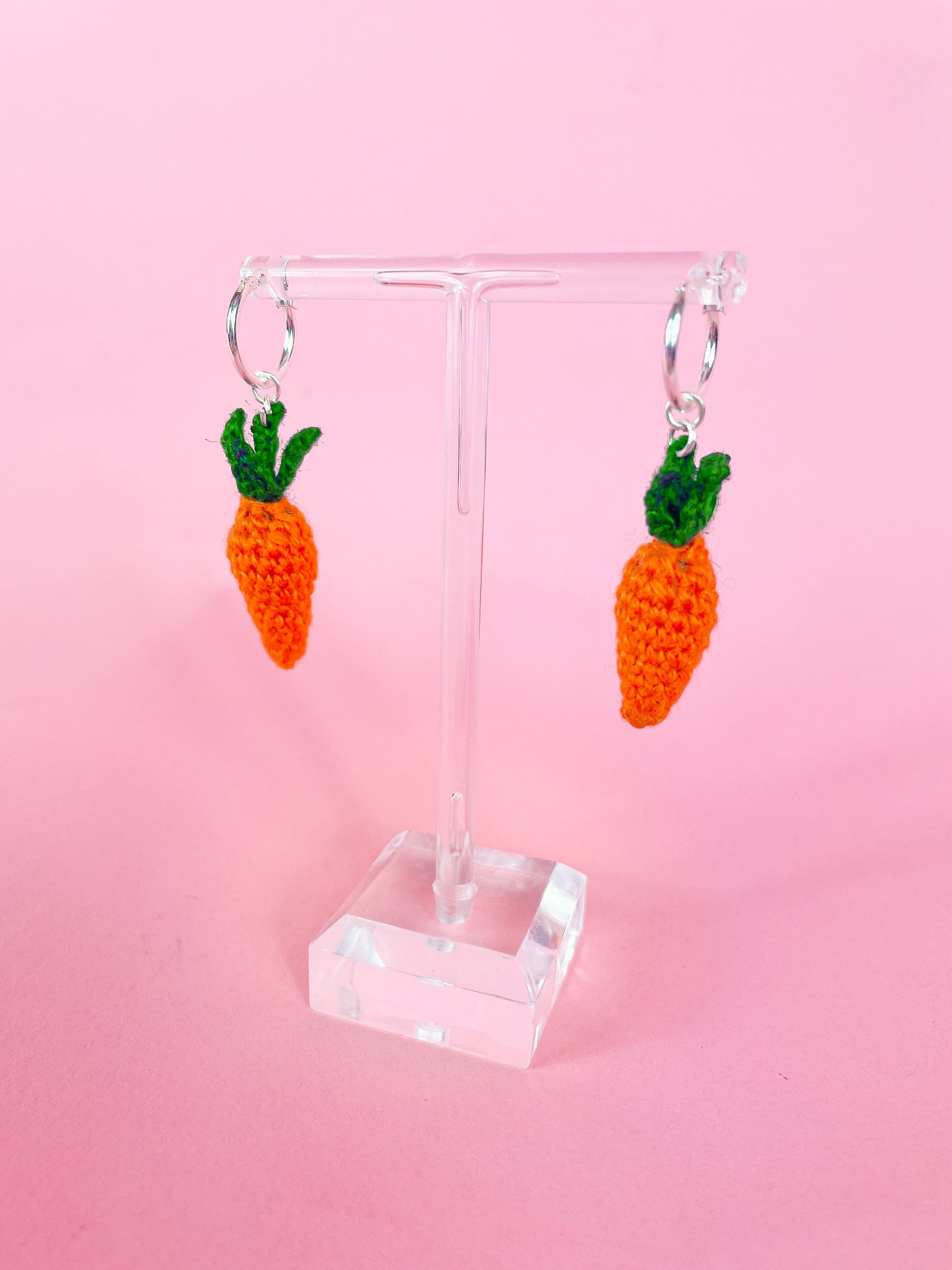 Side view of a pair of crochet carrot earrings attached to small silver hoops on an earring stand.