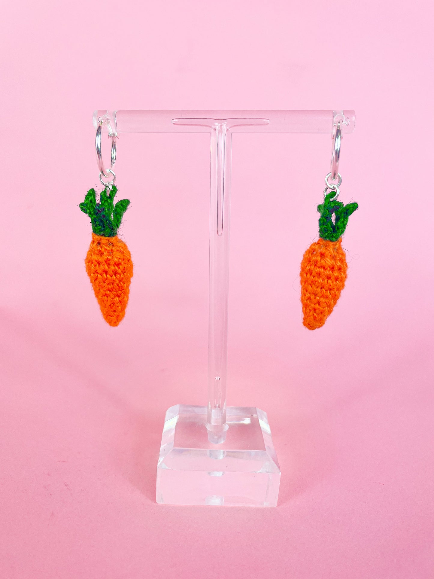 A pair of silver hoop earrings with crocheted mini carrots attached to them hung on an earring stand.