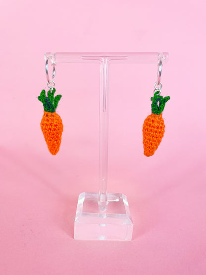 A pair of silver hoop earrings with crocheted mini carrots attached to them hung on an earring stand.