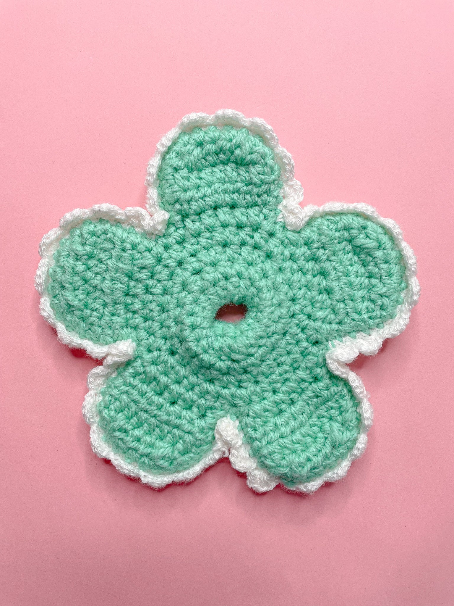 A daisy shaped green scrunchie lying flat on a pink background.