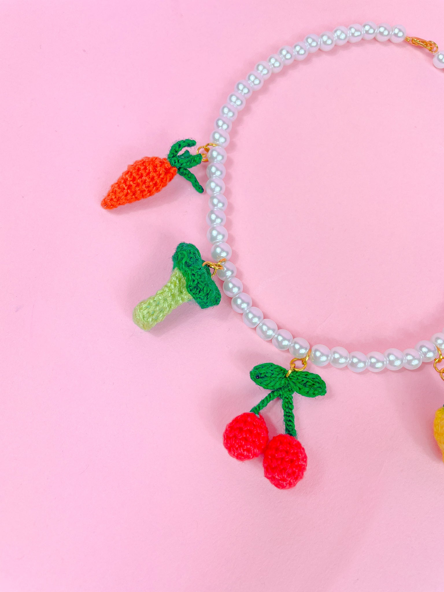 Flat lay close up of three of the crochet beads attached to a pearl necklace (carrot, broccoli and cherry), showing the stitch details.