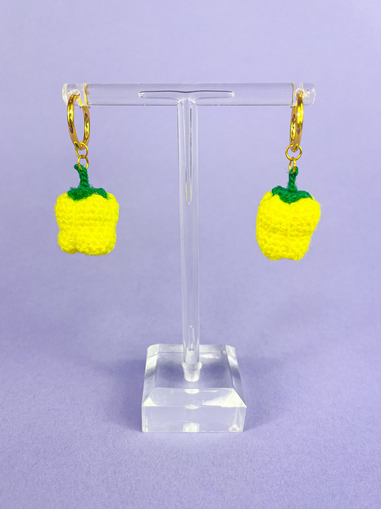 A pair of earrings with gold hoops and mini yellow bell peppers attached hung on an earring stand.