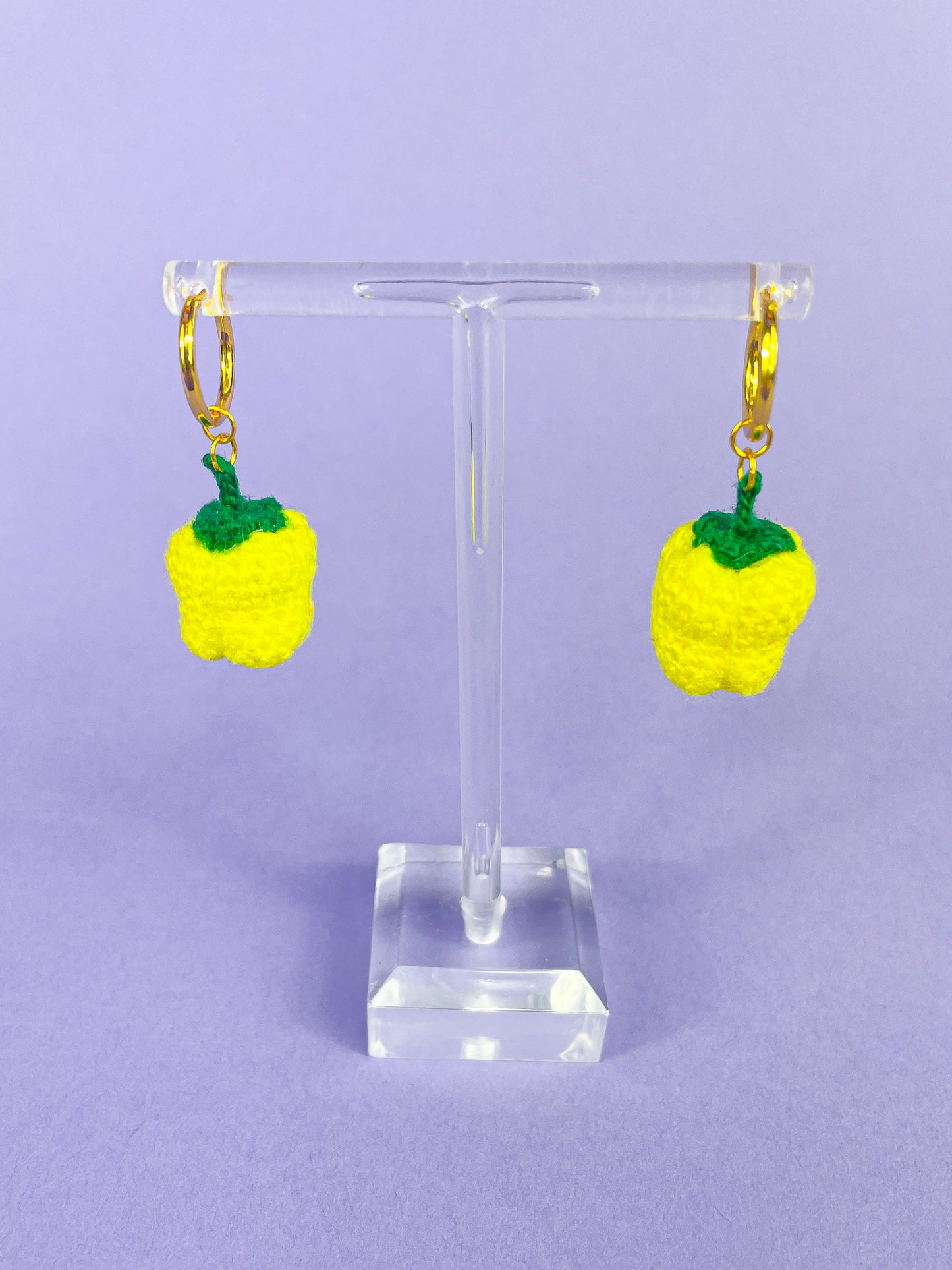 Above view of a pair of crochet bell pepper earrings hanging on 24k gold plated hoops displayed on an earring stand.