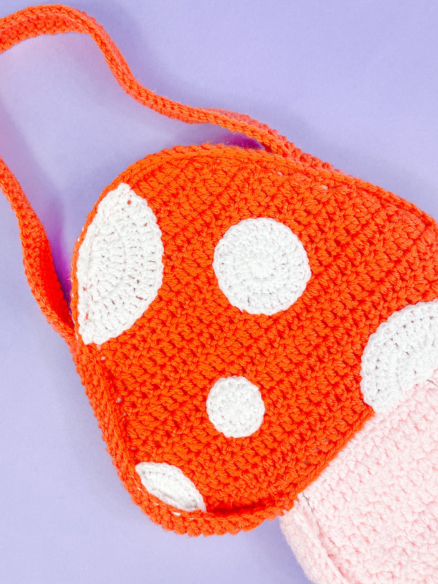 Close view of an orange mushroom bag with appliqué dots and showing the crochet stitches.