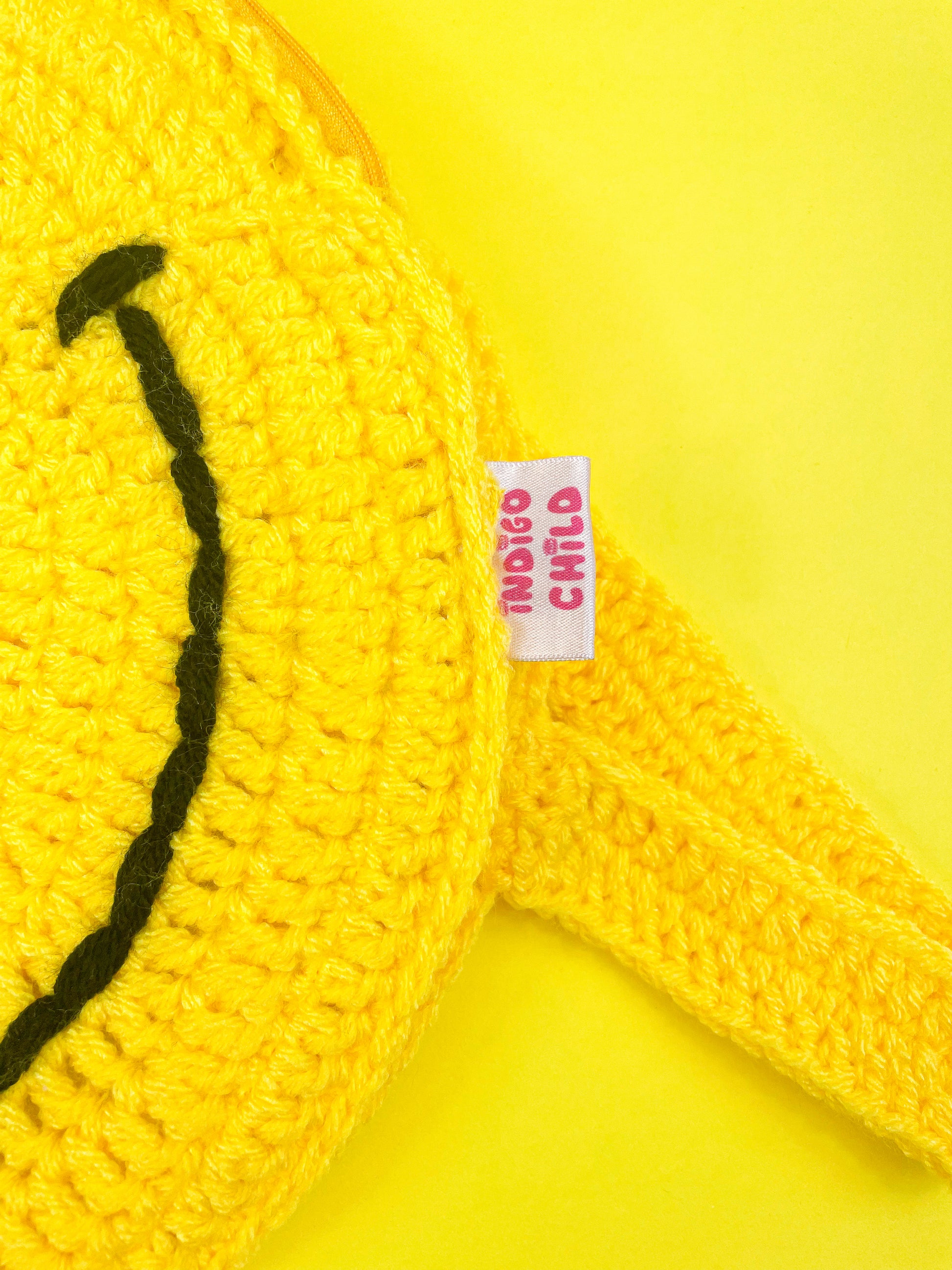 Close view of a yellow crochet bag lying flat with an Indigo Child tag sewn into the side.