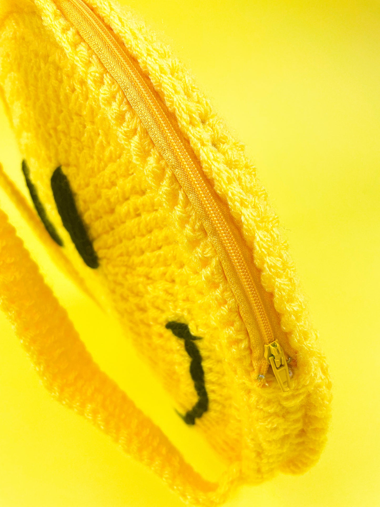 Close side view of a yellow crochet bag showing the crochet stitches and zipper.