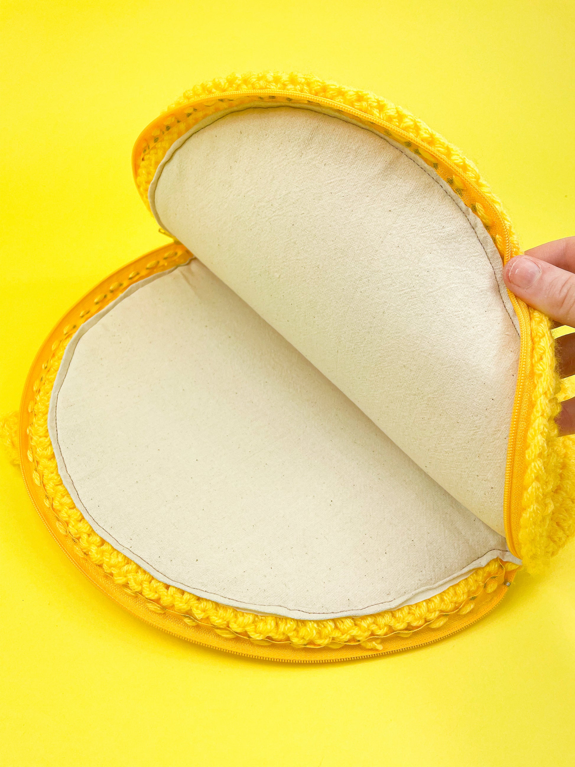 A hand holding the top of a bag open showing the inside of the bags lining and the zipper.