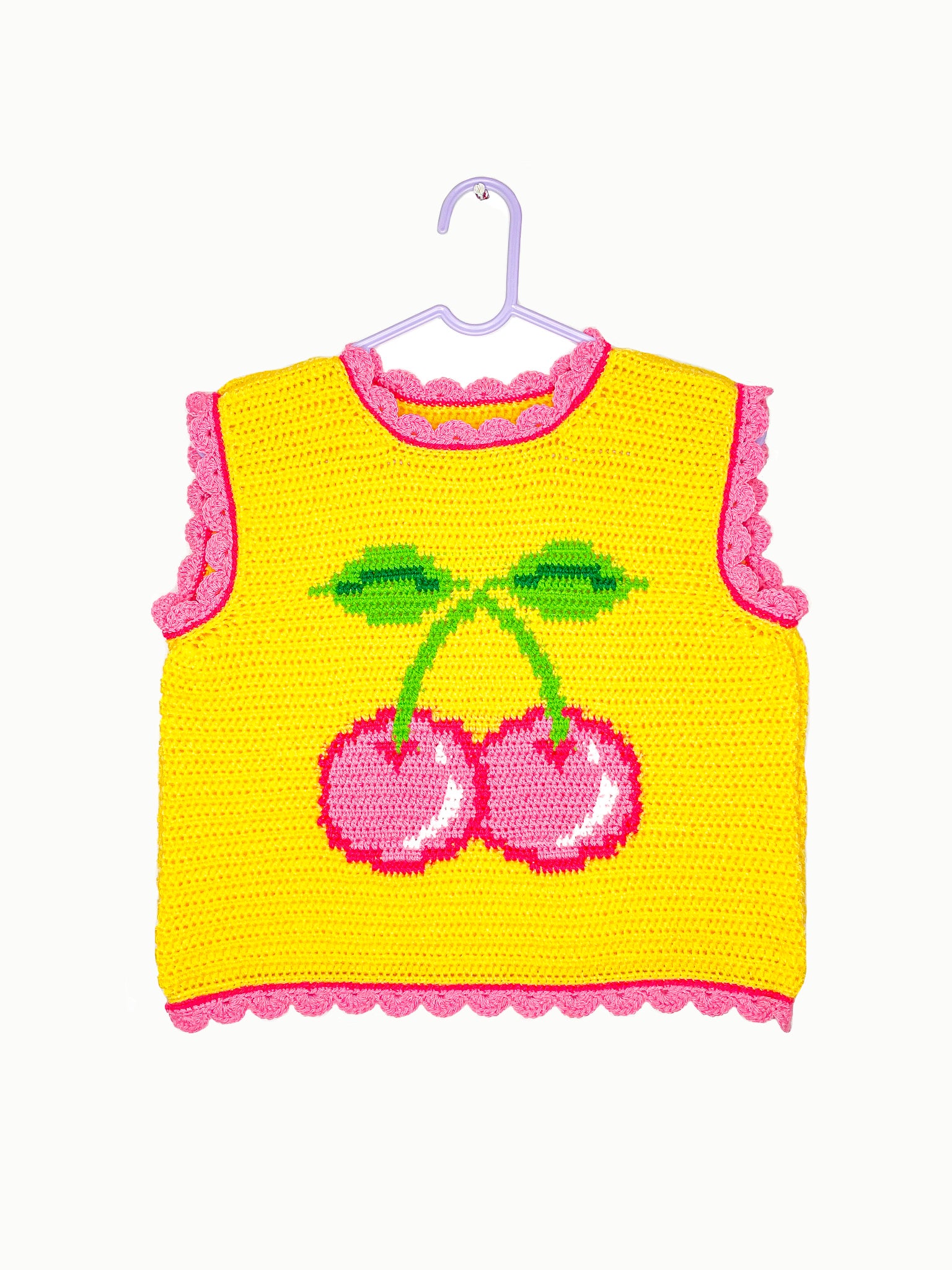 A yellow vest top with a pink cherry on the front and frills hung up on a white wall.