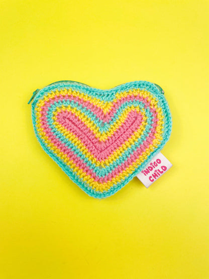 A heart shaped coin purse with a rainbow pansexual flag design (pink, yellow and aqua blue) lying on a yellow background.