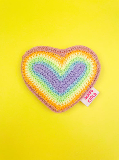 A pastel rainbow heart shaped purse lying on a yellow background with an outer tag sewn into it.