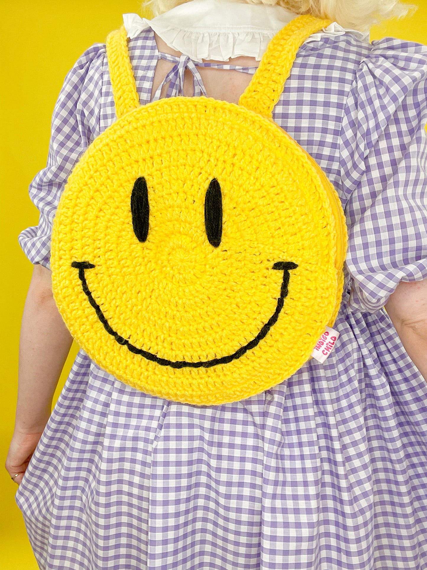 Back close view of woman wearing a smiley face backpack on her back showing the crochet stitches.