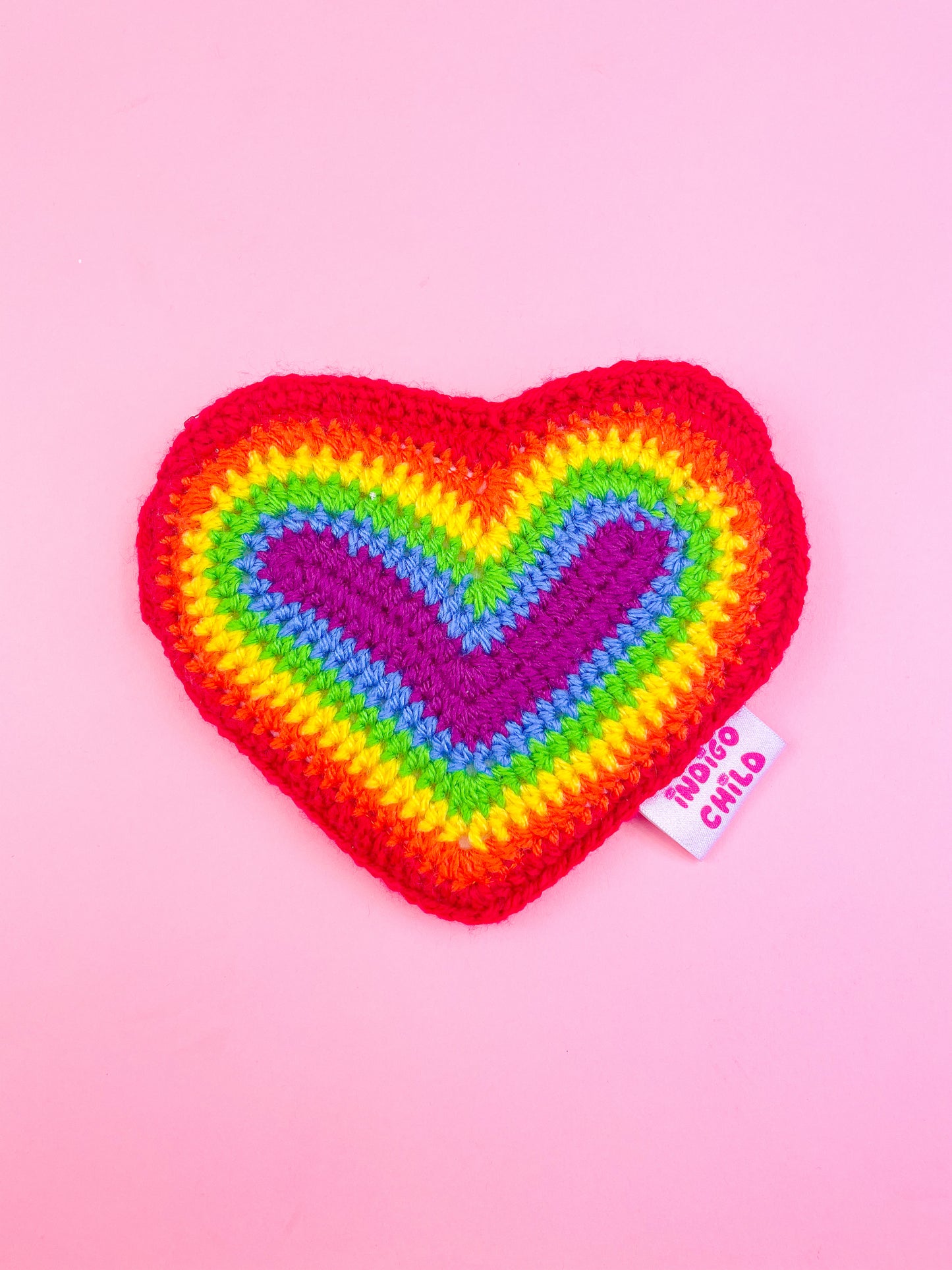 A rainbow crochet coin purse shaped like a heart with an Indigo Child logo tag attached.