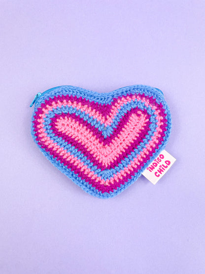 Heart shaped purse in the bisexual flag colours (pink, purple and blue) with a sewn Indigo Child outer tag, lying flat on a purple background.