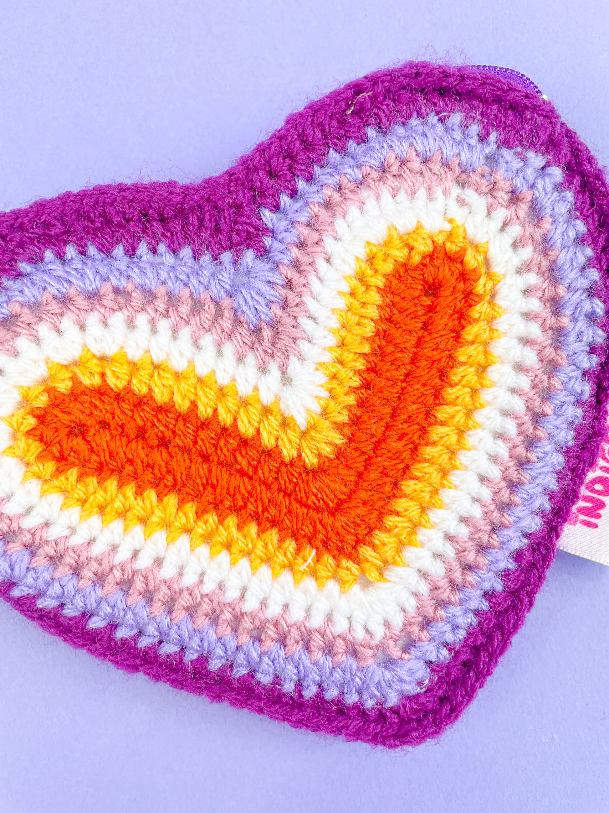 Close view of a coin purse shaped like a heart resembling the lesbian flag colours (orange, white, pink and purple) showing the crochet stitches.