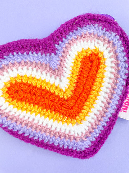 Close view of a coin purse shaped like a heart resembling the lesbian flag colours (orange, white, pink and purple) showing the crochet stitches.