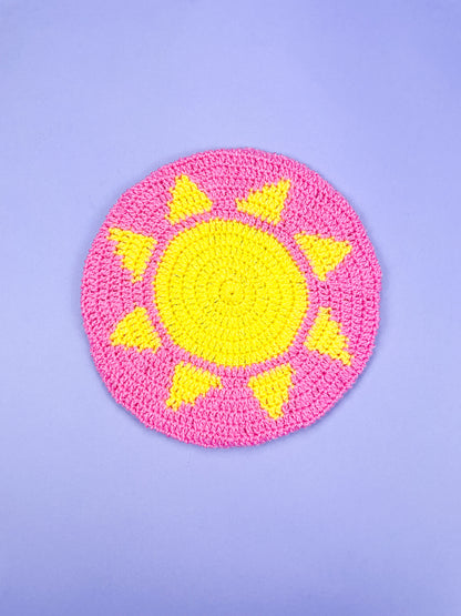 A pink beret with a yellow sun in the centre placed on a purple background.