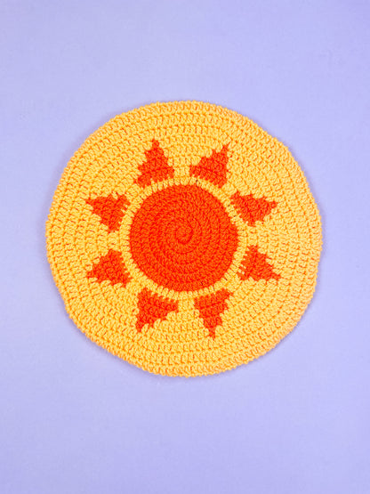 A yellow beret with an orange sun on the base lying on a purple background.