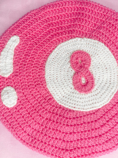 Close view of a beret in pink with crochet appliqué attached to the base to resemble an 8 ball and showing the crochet stitches.