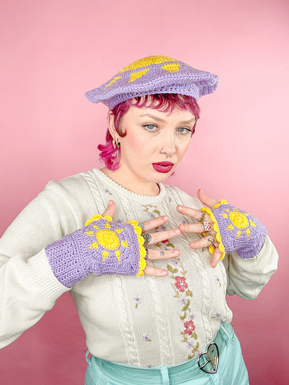 A woman posing wearing a pair of lilac crocheted gloves with suns on them and a matching beret, paired with a granny style jumper.