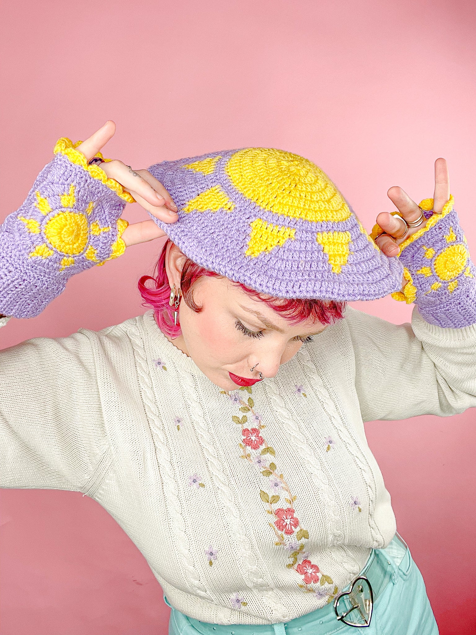 Side view of woman posing wearing a purple beret with a sun on it and matching purple gloves with yellow suns.