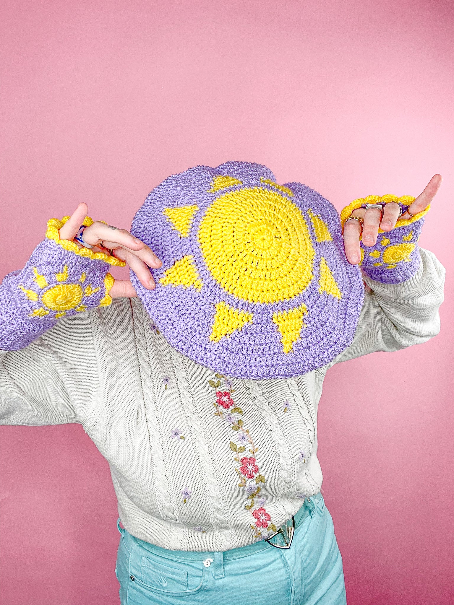 Above view of a woman wearing a lilac crochet beret with a yellow sun on the top paired with matching gloves.