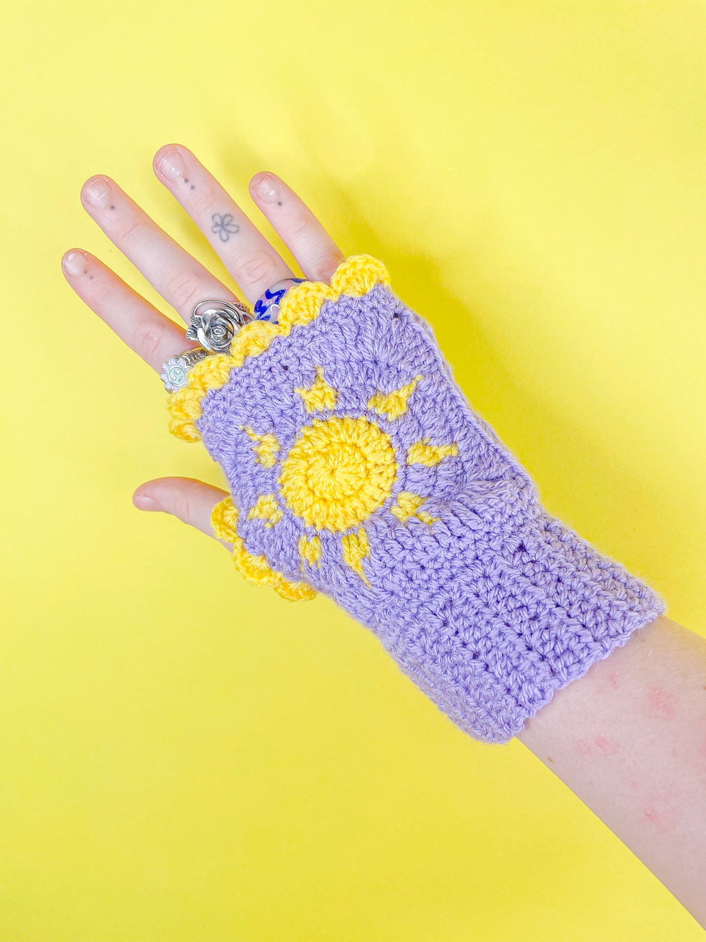 One hand wearing a sun fingerless glove in purple with a yellow frilly edge.