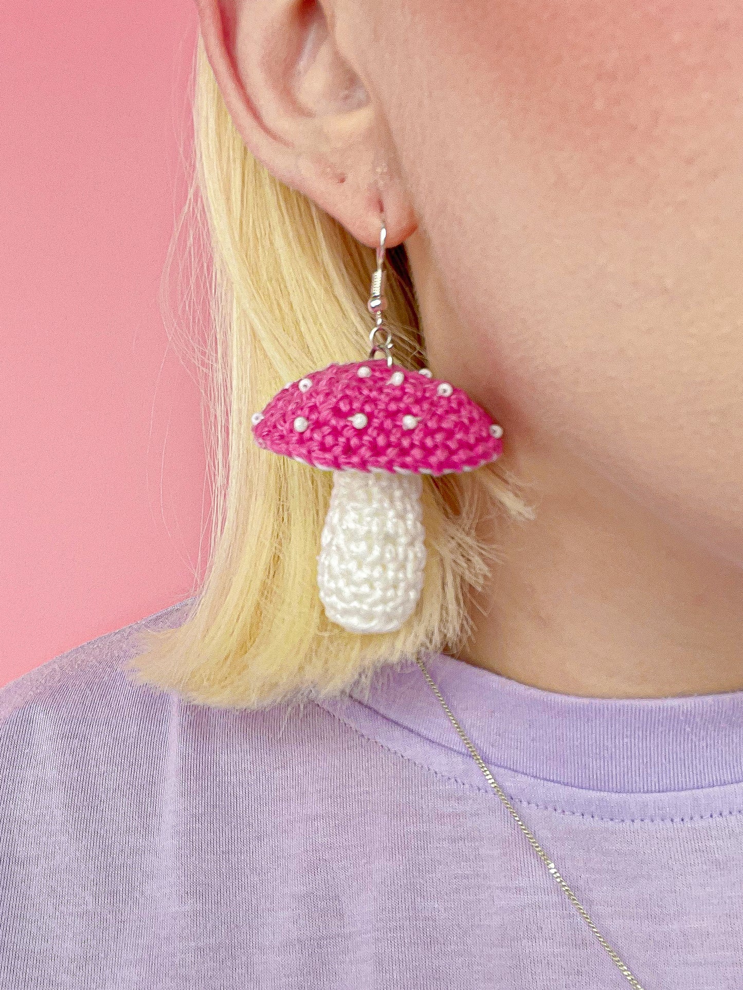 Close view of a woman wearing one mushroom shaped earring in pink with white seed beads attached resembling the toadstool dots.