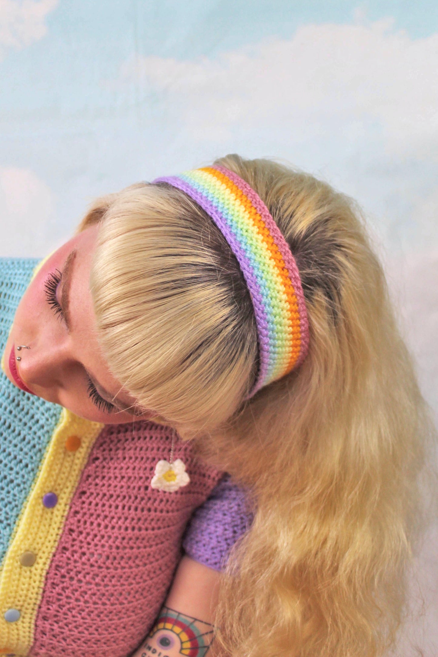 Above view of a woman wearing a pastel rainbow headband with a matching patchwork pastel top in front of a cloud background.