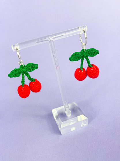 Above side view of a pair of mini crochet cherry earrings.