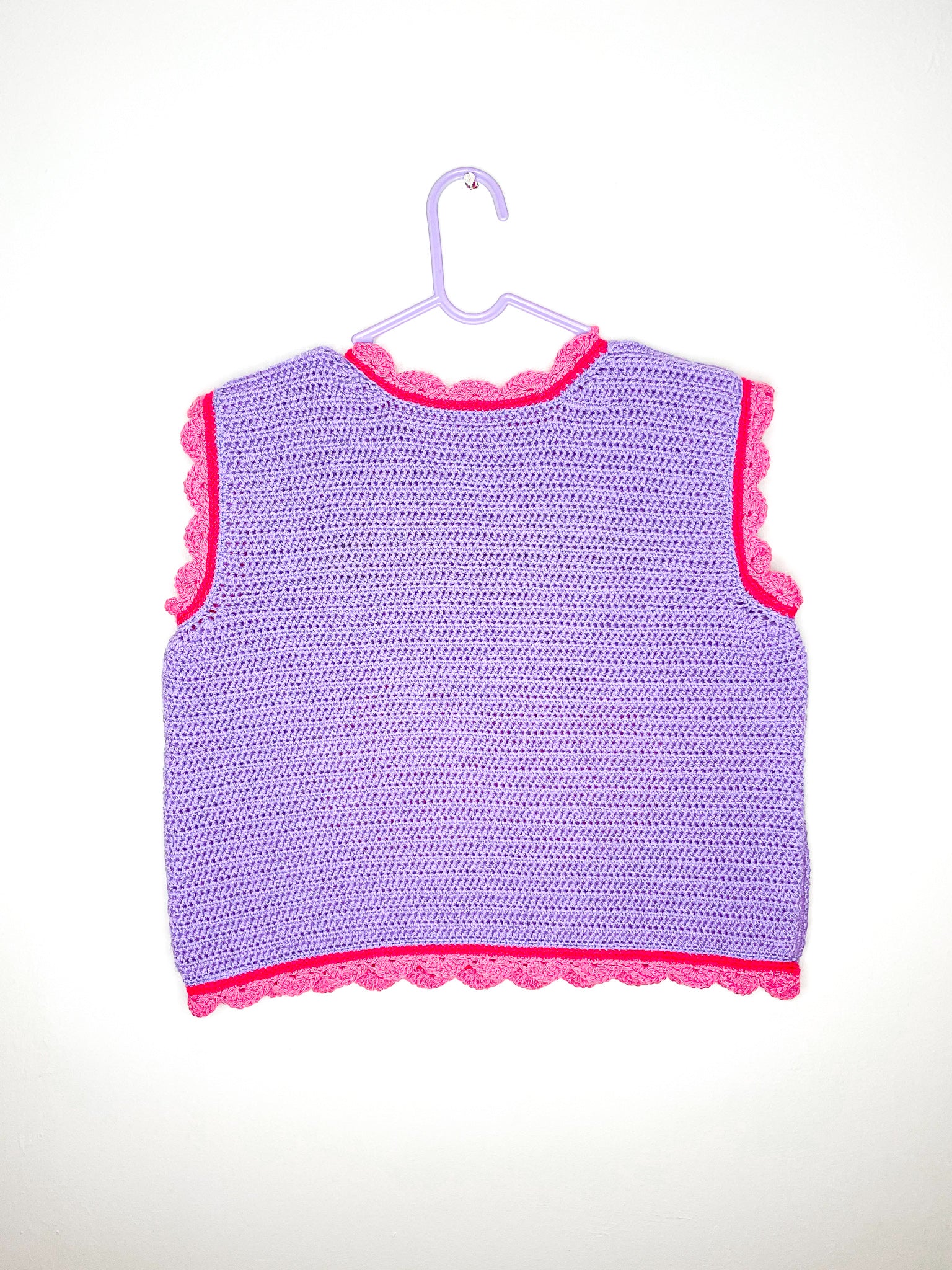 Back view of a purple vest top with pink frilly edges hung on a white wall.