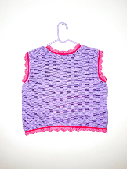 Back view of a purple vest top with pink frilly edges hung on a white wall.